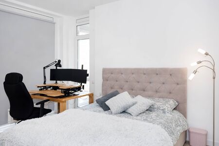 Bedroom interior with a study corner. Large double bed and a desk with a computer and a rolling chair. Home office, freelance workの写真素材