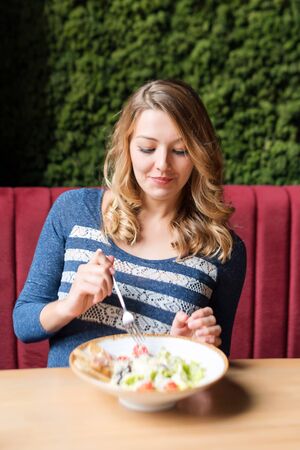 Blonde pretty woman eating salad. Client tasting delicious meal in a restaurant.の写真素材