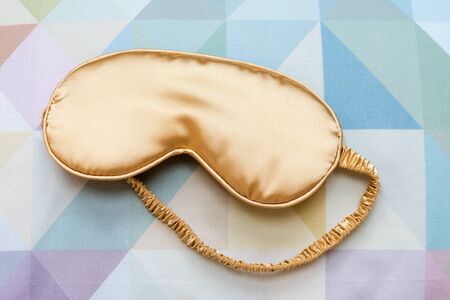 Golden sleeping eye mask on the bed, top view. Good night, flight and travel concept. Sweet dreams,...