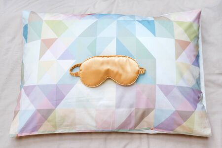 Golden sleeping eye mask on the bed, top view. Good night, flight and travel concept. Sweet dreams,...