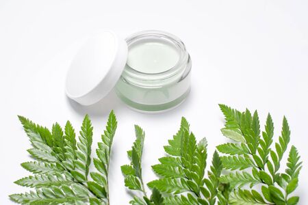 Cosmetic cream in container and fresh green leaves on white background. Homemade spa, jar of organic...