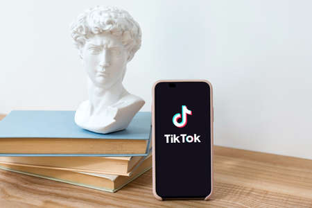Kyiv, Ukraine - May 28, 2020: TikTok application logo on Iphone X screen on wooden table with books...