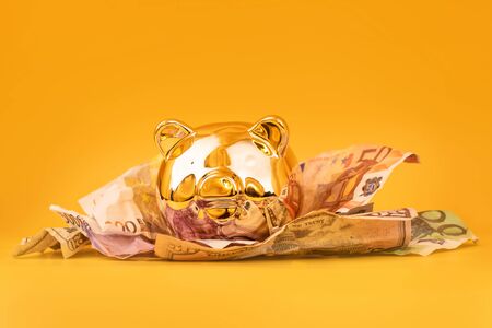 Golden piggy bank with cash money, euro and dollar banknotes. Golden money box, huge savings, money accumulation. Money saving, moneybox, finance and investments, budget concept. Copyspace.の写真素材