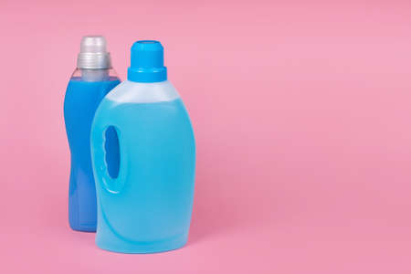 Bottles of detergent and fabric softener on pink background. Containers of cleaning products, household chemicals. Liquid laundry detergent and conditioner. Laundry day, washing and cleaning conceptの写真素材