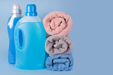Bottles of detergent and fabric softener with clean towels on blue background. Containers of cleaning products, household chemicals. Liquid detergent and conditioner. Laundry day, cleaning conceptの写真素材