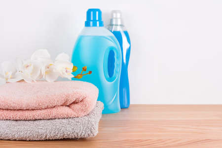 Bottles of detergent and fabric softener with clean towels and orchid flowers on wooden table. Containers of cleaning products. Liquid detergent and conditioner. Laundry day, cleaning concept.の写真素材
