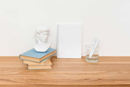 Empty notebook on wooden table with books and small David plaster copy made in China bust sculpture....