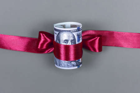 Hundred dollar bill tied with red bow on grey background. Money, gift wrapped in red bow and ribbon, US currency, cash, business success, bonus, monetary prize, luck in the game conceptの写真素材