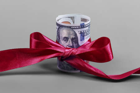 Hundred dollar bill tied with red bow on grey background. Money, gift wrapped in red bow and ribbon, US currency, cash, business success, bonus, monetary prize, luck in the game conceptの写真素材