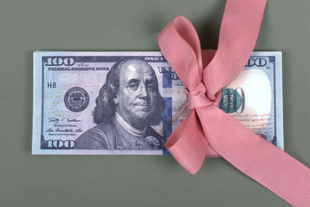 Hundred dollar bill tied with pink bow on grey background. Money, gift wrapped in pink bow and ribbon, US currency, cash, business success, bonus, monetary prize, luck in the game conceptの写真素材