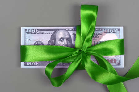 Hundred dollar bill tied with green bow on grey background. Money, gift wrapped in green bow and ribbon, US currency, cash, business success, bonus, monetary prize, luck in the game conceptの写真素材