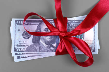 Hundred dollar bill tied with red bow on grey background. Money, gift wrapped in red bow and ribbon, US currency, cash, business success, bonus, monetary prize, luck in the game conceptの写真素材