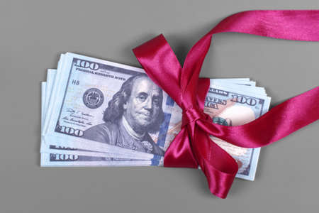 Money as gift concept, win or bonus, hundred dollar bills on grey background. Pile of 100 dollar bills is tied with red ribbon with bow.の写真素材