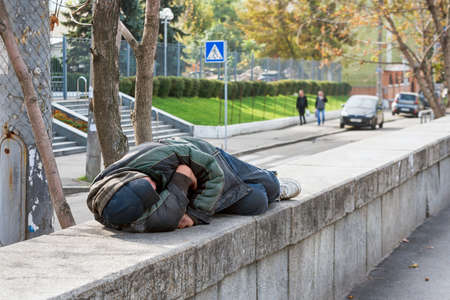 Poor homeless man or refugee sleeping on the street in the city. Problems of urban life in big modern cities, social documentary concept, selective focus.の写真素材