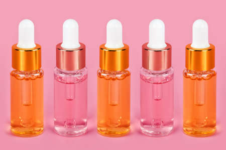 Row of skin care essence oil dropper glass bottles on pink background. Hydrating serums, vitamins for skin. Anti aging serum with collagen and peptides in bottle with dropper. Aesthetic, minimalismの写真素材