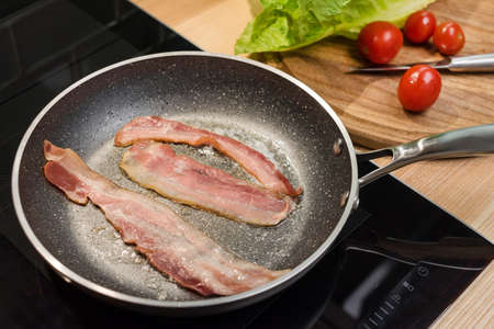 Slices of fresh fried bacon in a pan for breakfast, ingredients for chicken caesar salad, cooking on...