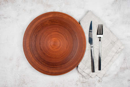 Empty plate and cutlery on a napkin. Dinner setting, ceramic plate and silverware over light table background. Top view, copyspace.の写真素材