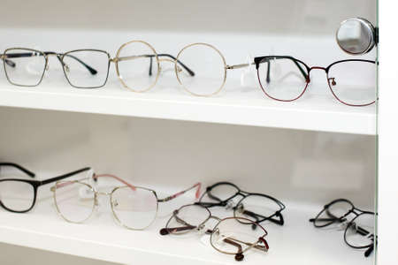 Eyeglasses in optical store, fashion, different glasses on white shelf in shopping mall. Selective focus.の写真素材