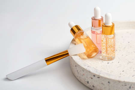 Hydrating anti aging serum with collagen and peptides in glass bottle with dropper. Skin care essence glass bottles on marble cosmetic tray on light background. Vitamins for skin. Cosmetic conceptの写真素材