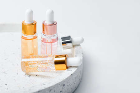 Hydrating anti aging serum with collagen and peptides in glass bottle with dropper. Skin care essence glass bottles on marble cosmetic tray on light background. Vitamins for skin. Cosmetic conceptの写真素材