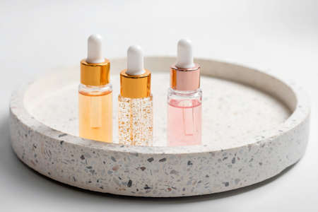 Hydrating anti aging serum with collagen and peptides in glass bottle with dropper. Skin care essence glass bottles on marble cosmetic tray on light background. Vitamins for skin. Cosmetic conceptの写真素材