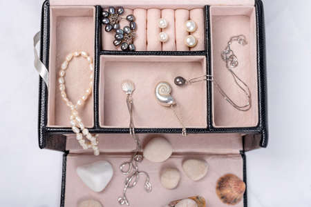 Sea jewelry collection in jewelry box on light marble background with seashells and pebbles. Pearl pendant necklace, pearl earrings and silver chains. Fashion flat lay, ocean summer jewelryの写真素材