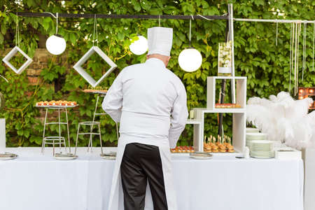 Chef decorating food on the table for guests outdoors. Wedding catering, buffet. Serving food on...