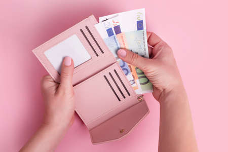Hands holding wallet. Pink leather wallet with euro money in female hands. Closeup on a woman's hands taking European bank notes out of purse and counting. Concept of money, finances, shopping, cashの写真素材