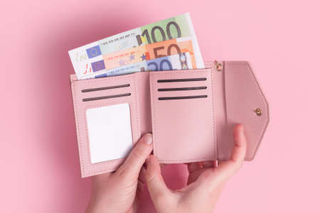 Hands holding wallet. Pink leather wallet with euro money in female hands. Closeup on a woman's hands taking European bank notes out of purse and counting. Concept of money, finances, shopping, cashの写真素材