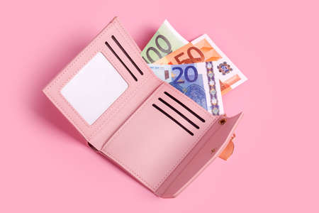 Pink purse on pastel pink background with euro bills in it. Closeup of opened modern leather wallet and european banknotes. Finance, investment, saving, cash, hopping and payment concept. Top view.の写真素材