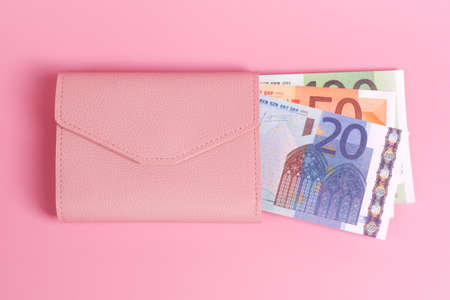 Pink purse on pastel pink background with euro bills in it. Closeup of modern leather wallet and european banknotes. Finance, investment, saving, cash, hopping and payment concept. Top view.の写真素材