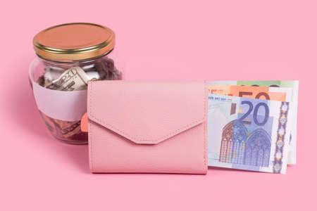American dollars in glass money jar with blank label and pink wallet full of euro banknotes, financial, saving, exchange, diversification. Jar full of cash, saving money, expense planning and control.の写真素材