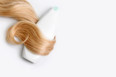 Shampoo or conditioner bottle wrapped in lock of curly blonde hair isolated on light background, top view. Flat lay, copy space for text. Hair care cosmetics, beauty haircare products, hair treatmentの写真素材