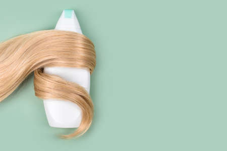 Shampoo or conditioner bottle wrapped in lock of curly blonde hair on light mint background, top view.Flat lay in pastel colors, mockup. Hair care cosmetics, beauty haircare products, hair treatmentの写真素材