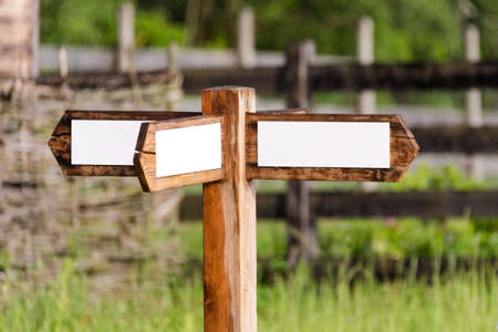 Empty wooden sign with arrows on the ranch. Simple wooden triple direction arrow roadsign in the gargen with wooden fenceの写真素材