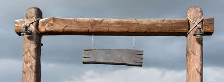 Empty wooden signboard suspended from wooden poles. Blank wood sign with copyspace ready for your text message, hanging on pole at side of rural country road, bannerの写真素材