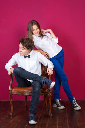 Teenage girls wearing jeans and sneakers posing on painted pink wall background in loft apartment. Teenagers in white shirts posing in loftの写真素材