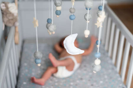 Baby crib mobile with stars, planets and moon hang over the sleeping newborn. Kids handmade toys above the newborn crib. First baby eco-friendly toys made from felt and woodの写真素材