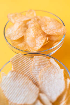 Potato chips in glass bowls on yellow background. Junk unhealthy food, chips, party food, fast food...
