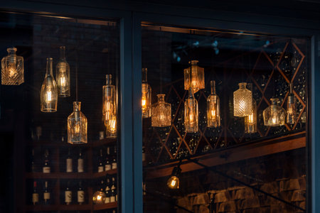 Lanterns made of glass bottles and Edison lamp bulbs. DIY lamps made from recycled old bottles hanging in cafe windowの写真素材