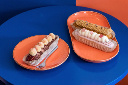 Eclairs in paper cases served on plates with a cake fork on cafe table. Delicious fresh cakes with...