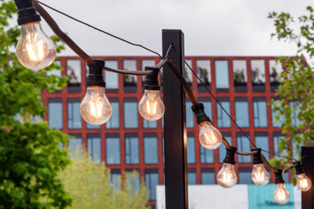 Light garland on the street at daylight. Decoration of the street with vintage Edison bulbs garland,...