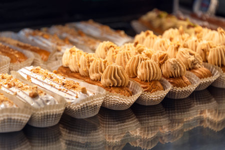 Eclairs on the shelf of a pastry shop or cafe. Tasty french sweets on window shop, delicious pastries for coffee. Cakes in pastry shop, variety of desserts with creamy topping on display in bakery.の写真素材