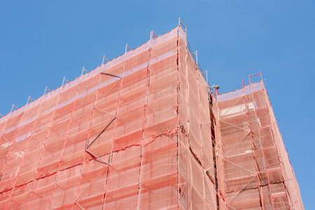 Building facade corner under construction is covered with a protective construction mesh. Building...
