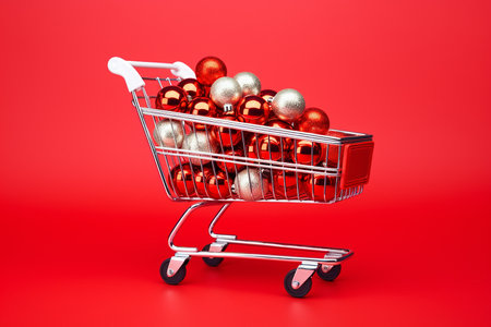 Shopping card full of Christmas balls. Supermarket trolley with decoration for winter holidays. Christmas and New Year sale minimal concept. Miniature shopping cart with christmas toys, toy shopping cart.の素材
