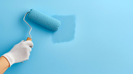 Hand painting wall with roller brush. Person applying bright blue paint to a wall with a roller. Banner template with copy space. Home improvements, renovations background textureの素材