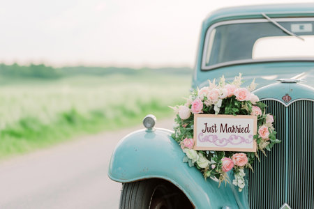 Wedding just married car decorated with flowers on a road. Classic vintage elegant bridal car, old-fashioned car. Floral wedding decorations, traditional festive celebrations, wedding dayの素材
