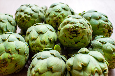 A detailed view of multiple green artichokes laid out on a table showcasing their texture. The image highlights the fresh, natural appearance of these vegetables, ideal for culinary, food, diet.の写真素材
