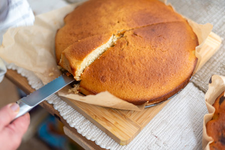 Close-up view of a person slicing a tender, golden-brown cake, freshly baked and placed on parchment...