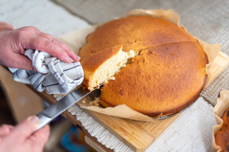 Close-up view of a person slicing a tender, golden-brown cake, freshly baked and placed on parchment...